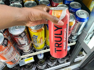 hand holding can of Truly in front of store refrigerator