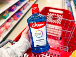 hand holding a bottle of colgate total mouthwash over a shopping cart
