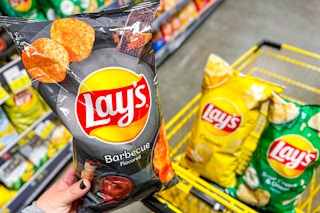 hand holding a bag of lays potato chips and bags of chips in shopping cart