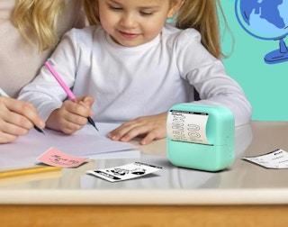 a parent and daughter drawing in a book with a sticker printer on a table