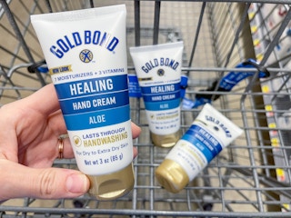 A Gold Bond Healing Hand Cream held out in front of other Gold Bond Healing Hand Creams sitting in the cart