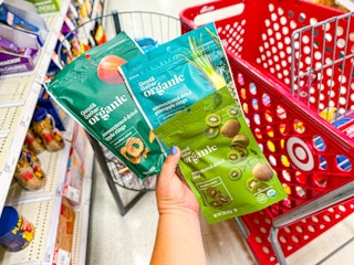 hand holding 3 good & gather organic dried fruit snacks in front of target cart