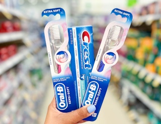 hand holding one box of Crest Pro-Health toothpaste and two Oral-B Manual Toothbrushes in aisle