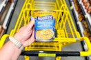 hand holding a can of progresso soup above a dollar general shopping cart