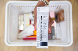 a hand holding a skincare in packaging over a shopping basket 