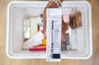 a hand holding a skincare in packaging over a shopping basket
