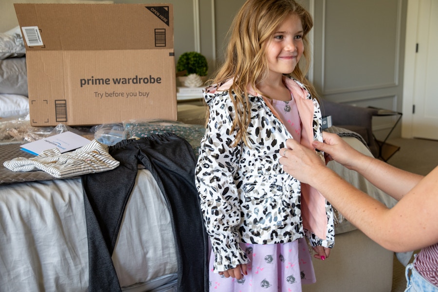 A woman helping a little girl try on a jacket to determine the fit.