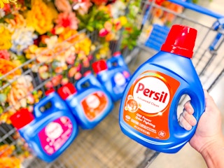 hand holding a bottle of persil detergent over walmart cart