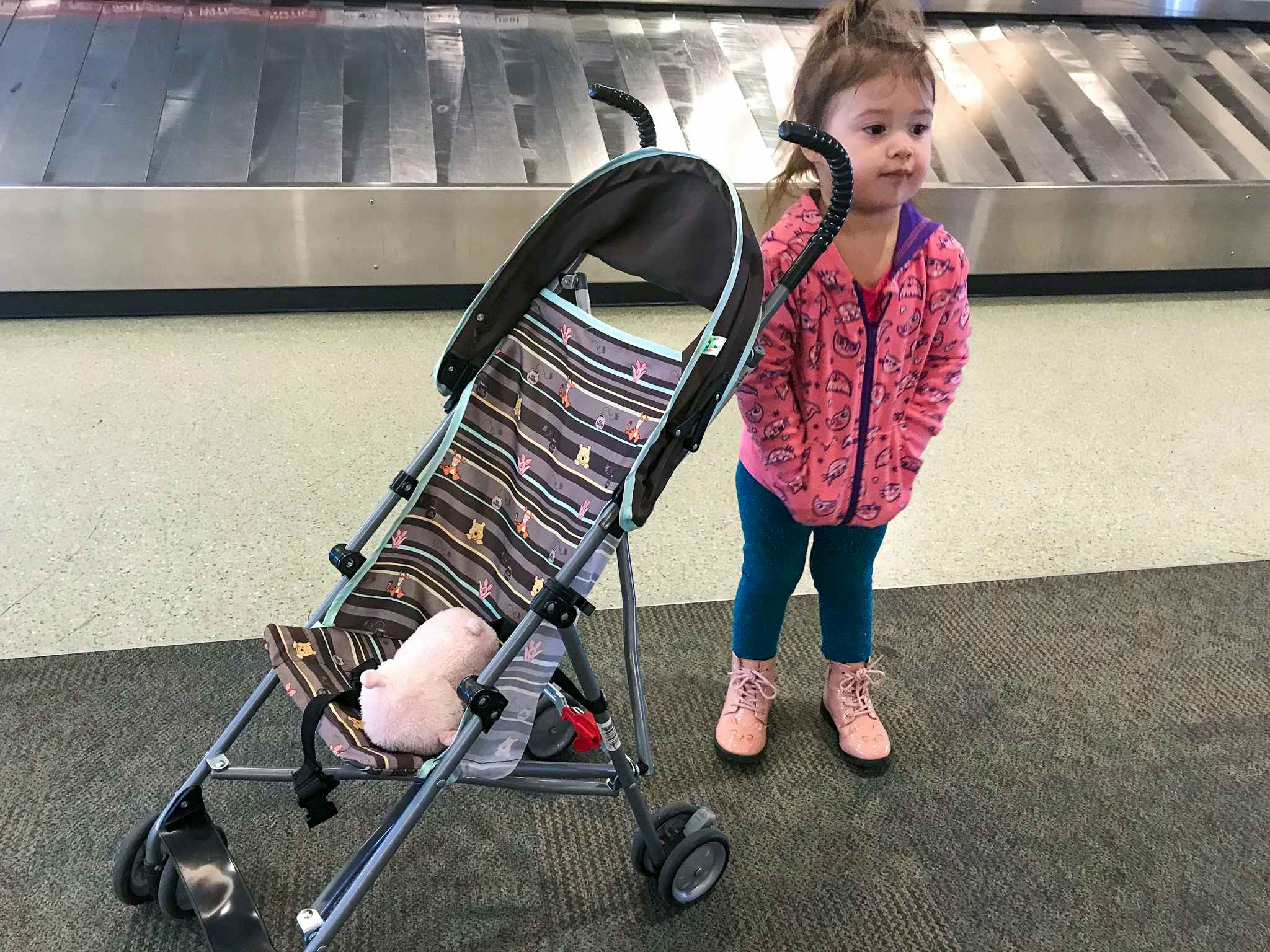 a little girl standing next to a stroller in an airport