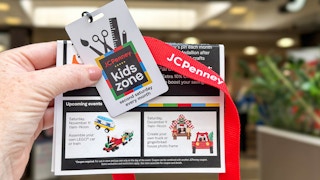 a person holding up a jcp kids workshop badge and flier in front of store