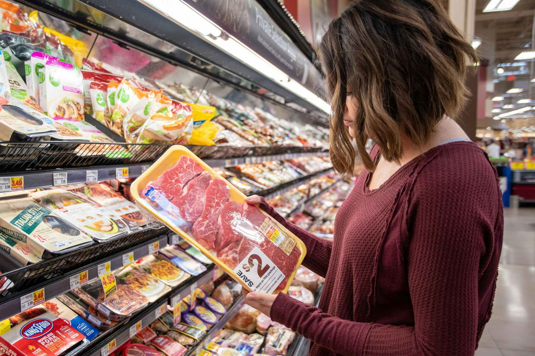 A person holding a pack of fresh meat while standing in front of fresh meat on store shelves.