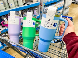 hand holding a blue tumbler in front of a green and lilac tumbler