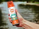 a hand holding an orange and white can of insect spray