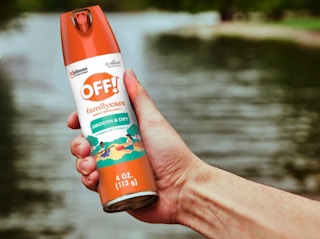 a hand holding an orange and white can of insect spray