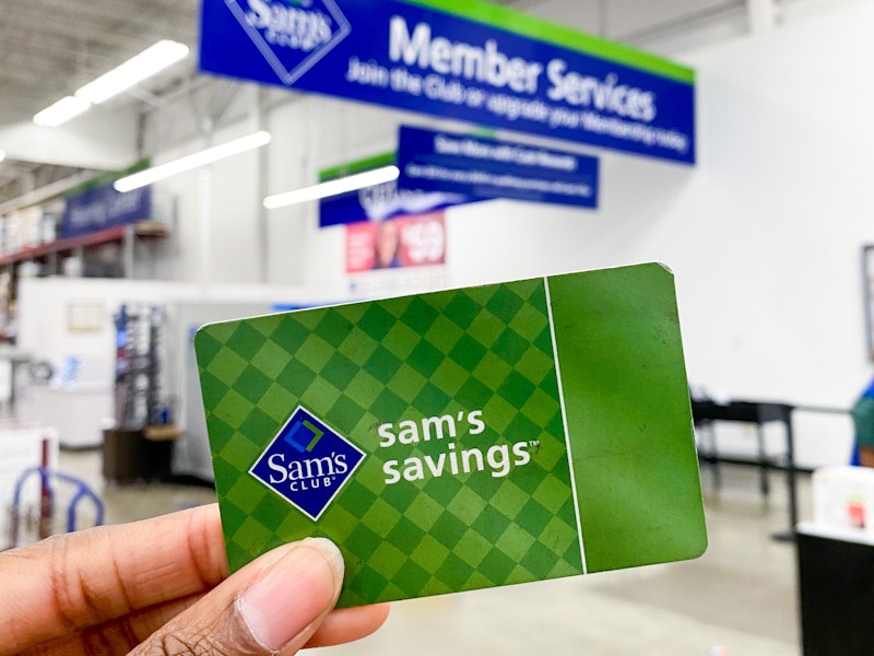 A person holding a Sam's Club membership card in front of the Member Services desk inside Sam's Club.