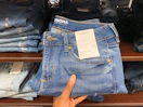 Hand holding a pair of Sonoma skinny jeans in front of a shelf with other jeans