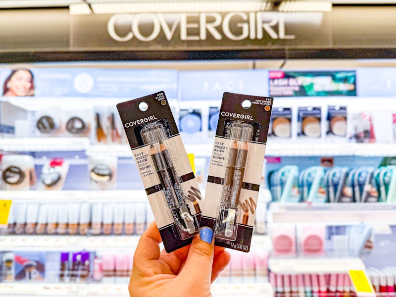 person holding 2 covergirl eyeliners in front of the covergirl display