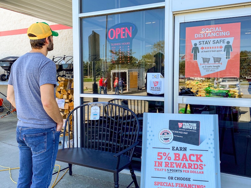 A man standing outside of Tractor Supply, looking at the hours.