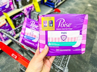 hand holding a pack of Poise pads in front of cart