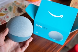 A person holding an amazon echo 4th generation device next to the box it came in.