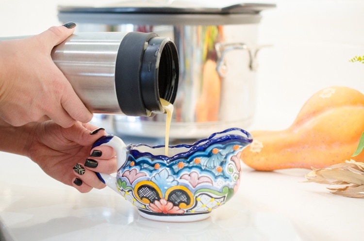 Someone pouring gravy from a thermos into a dish.