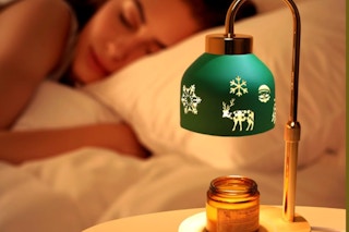  Loowoko Candle Warmer Lamp in the foreground of a woman sleeping in her bed.