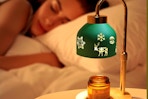 Loowoko Candle Warmer Lamp in the foreground of a woman sleeping in her bed.
