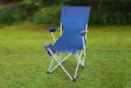 Lifestyle image of a blue Ozark Trail Camping Chair outdoors in a grass field 