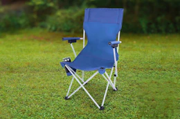 Lifestyle image of a blue Ozark Trail Camping Chair outdoors in a grass field 
