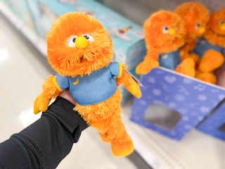 hand holding a ms rachel herbie doll in front of toys on a target shelf