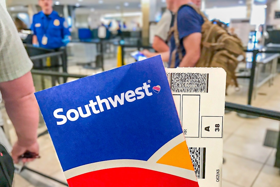 A Southwest airline ticket and envelope being held up while people are standing in line for TSA.