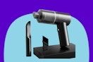 A small cordless rechargeable handheld vacuum cleaner leans against a wall. Next to it are a brush attachment and a crevice attachment.