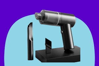 A small cordless rechargeable handheld vacuum cleaner leans against a wall. Next to it are a brush attachment and a crevice attachment.
