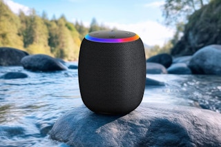 A wireless bluetooth speaker with RGB colors around the top sits in a rock in the water.
