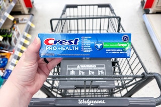 hand placing toothpaste into shopping cart in store aisle