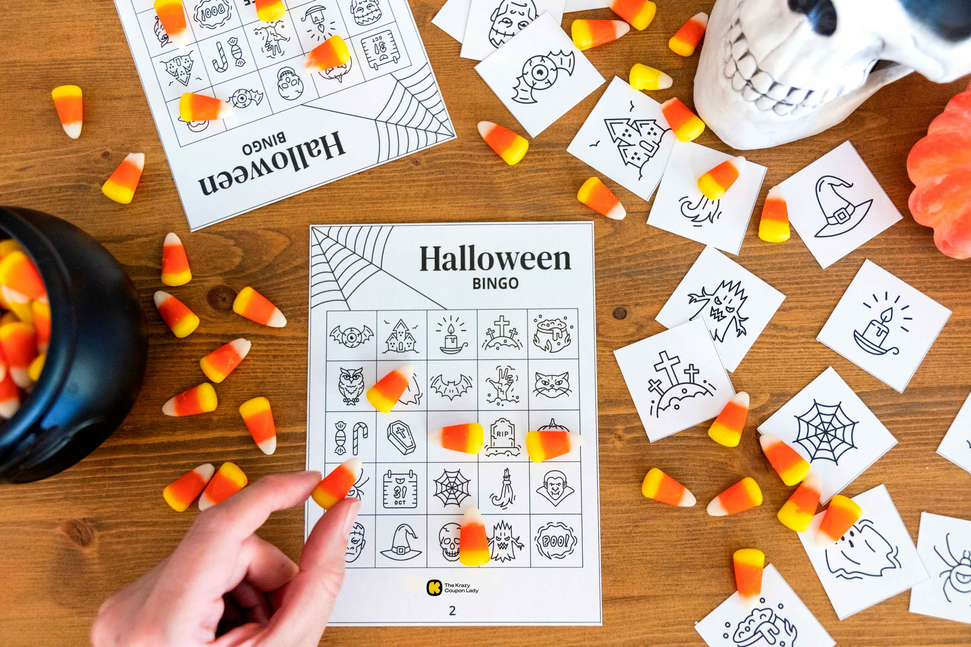 A person placing candy corn on a free printable Halloween bingo card with halloween decor in the background.