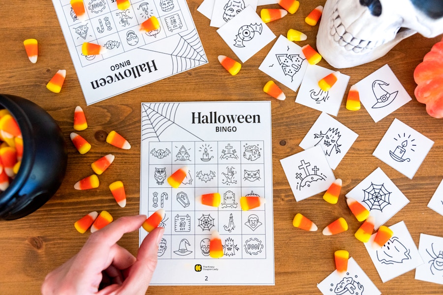 A person placing candy corn on a free printable Halloween bingo card with halloween decor in the background.