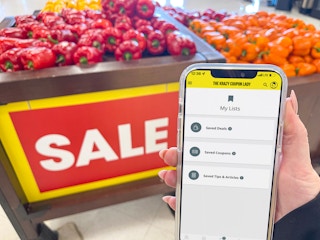a person holding a cellphone with kcl app in front of sale sign in store