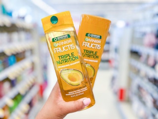 Hand holding a bottle of Garnier Fructis Triple Nutrition Shampoo and Conditioner in aisle