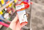 person holding sudafed nasal spray over a cart
