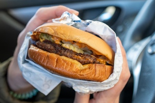 A close-up of a Sonic cheeseburger being held by someone sitting in a car.