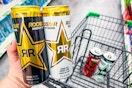 person holding 2 rockstar energy drinks over a cart with 2 more energy drinks in it