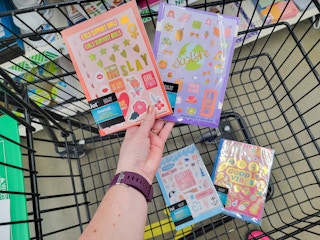 hand holding two journals with stickers in a cart with two more journals