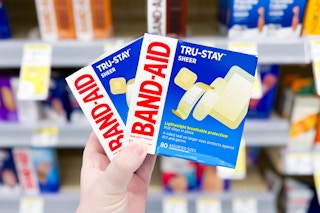 hand holding two boxes of band-aid tru-stay sheer bandages in front of first aid product shelves