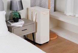 a beige laundry hamper next to a nightstand in a room