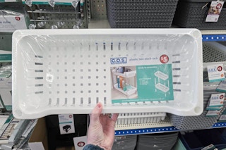 person holding an under sink organizer in front of shelves
