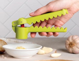 a green garlic press pressing garlic cloves in a bowl