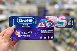 hand holding toothpaste and toothbrush in store aisle