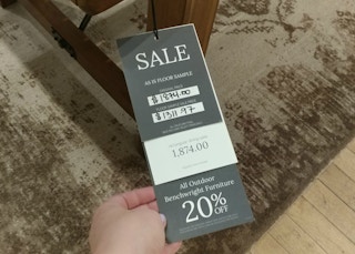 A woman's hand holding a sale tag on a Pottery Barn furniture item in store
