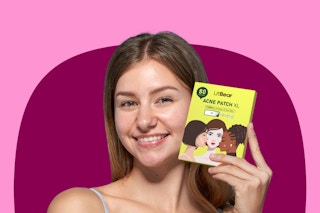 A young woman with straight brown hair and clear skin holds up the yellow box of pimple patches and smiles.